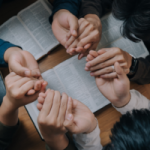 Group of people holding hands over the Bible in prayer for National Day of Prayer. By witsarut/Stock.Adobe.com.
