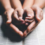 Parent holding child's hands over an open bible. By doidam10/stock.adobe.com. Pastor's six-year-old dies by tragedy on vacation. Lucy Morgan.